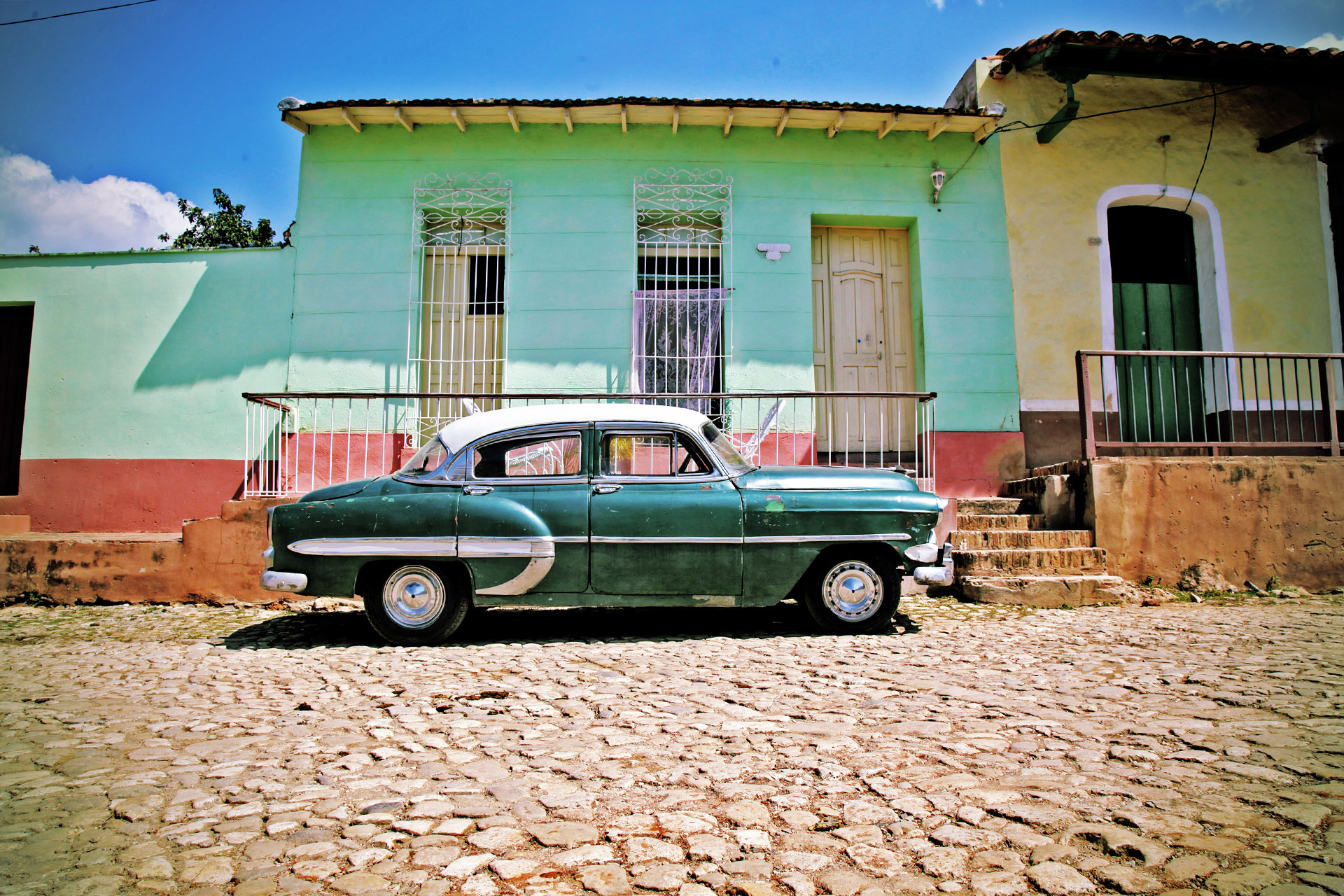 Grünes Oldtimer-Auto vor buntem Haus in Kuba